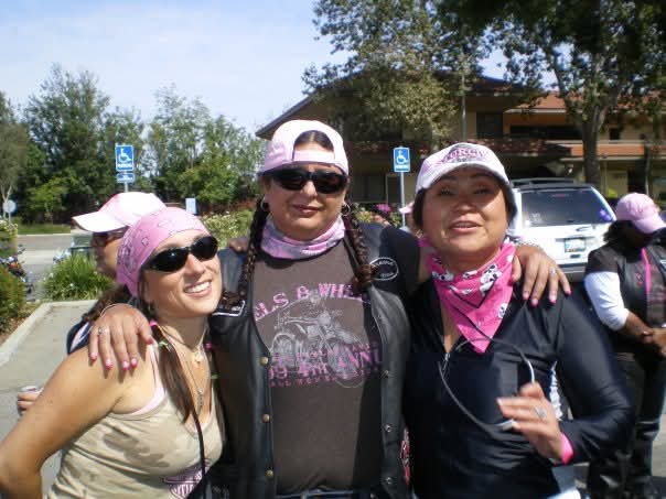 Three riders in pink bandanas and Heels & Wheels shirts smiling together
