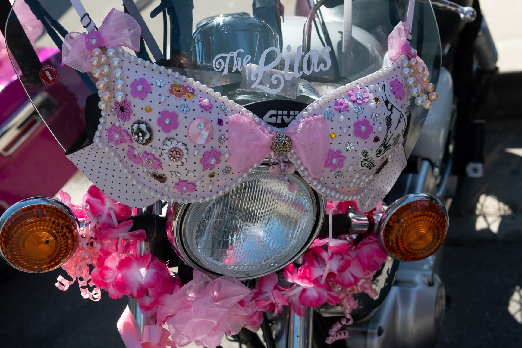 Decorated pink bra with pearls and flowers displayed on a motorcycle headlight