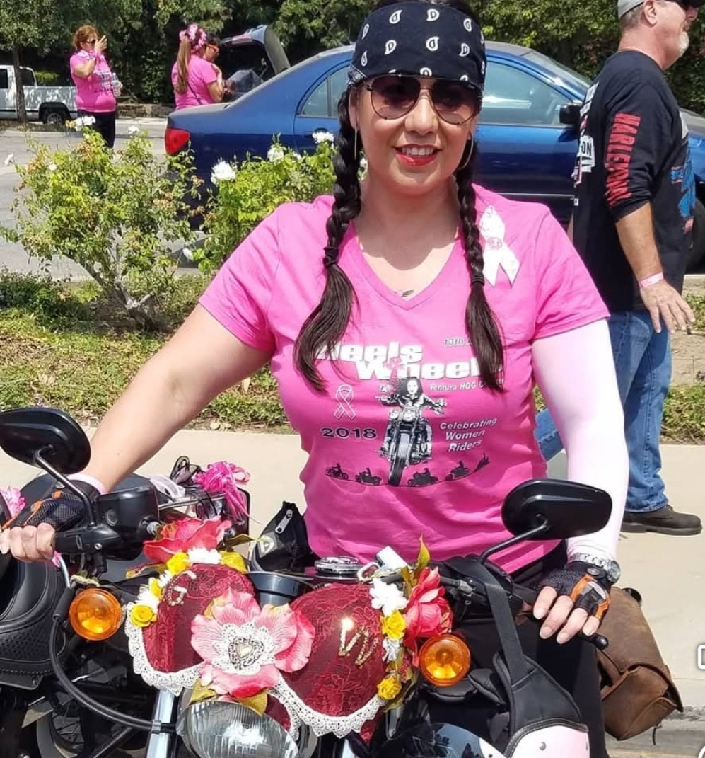 Rider in a pink Heels & Wheels shirt standing with her decorated motorcycle