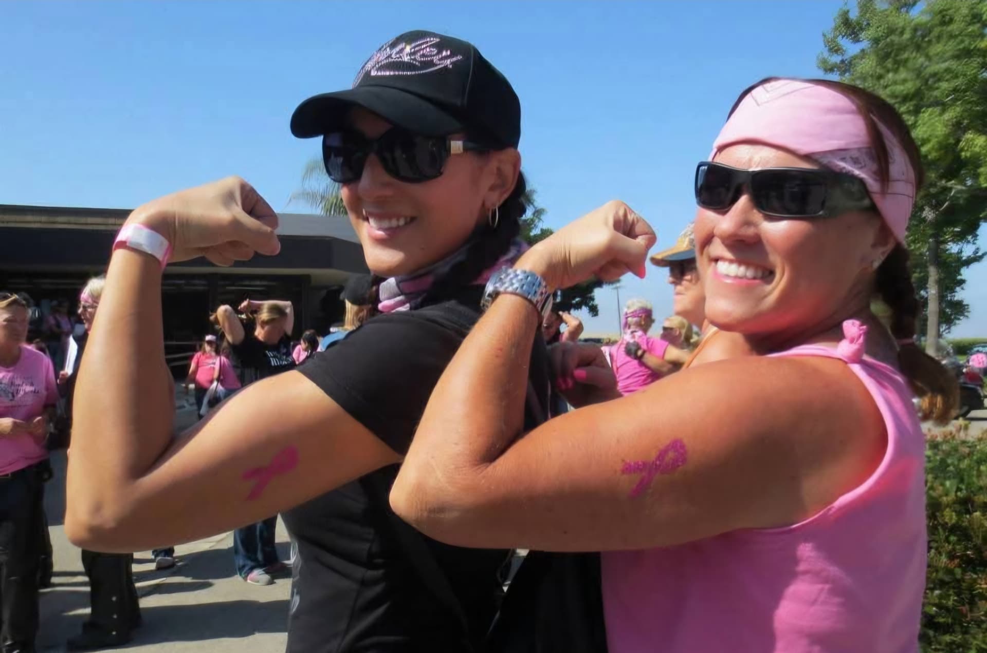 Two riders flexing their arms with pink breast cancer ribbons painted on them