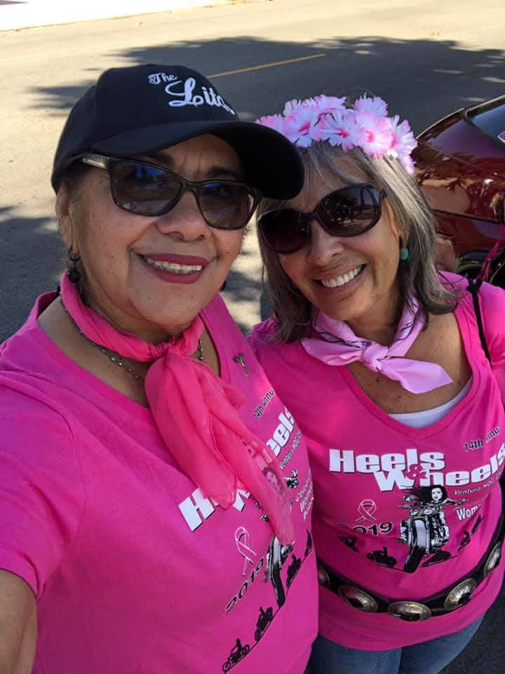 Two riders in 14th Annual Heels & Wheels shirts smiling in the sun